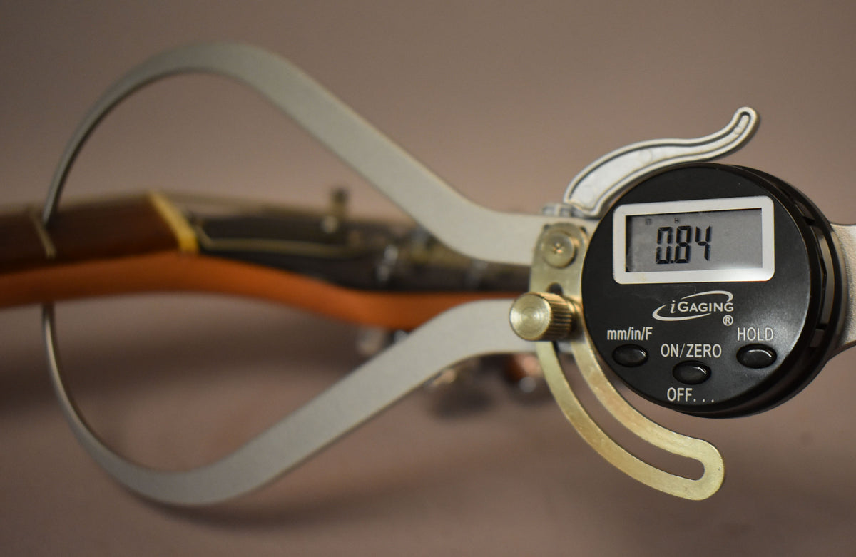 A digital caliper measures the guitar's neck thickness at the first fret, displaying "0.84" on its screen.