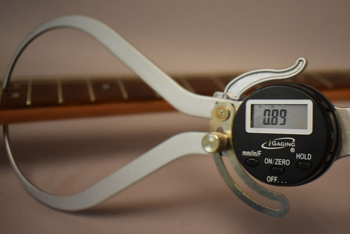 A digital caliper measures the string height at the 12th fret of the guitar's rosewood fretboard, reading 0.89.