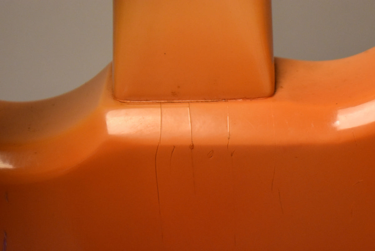 Close-up of the faded pink guitar's neck joint, showing finish checking and small dings on the body and neck heel.