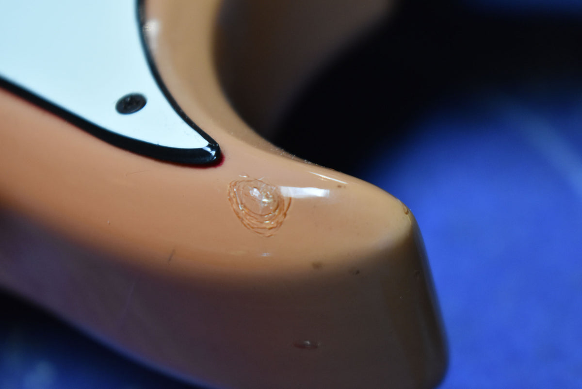 Close-up of the faded pink body with a large circular ding near the pickguard, showing concentric rings of damage.