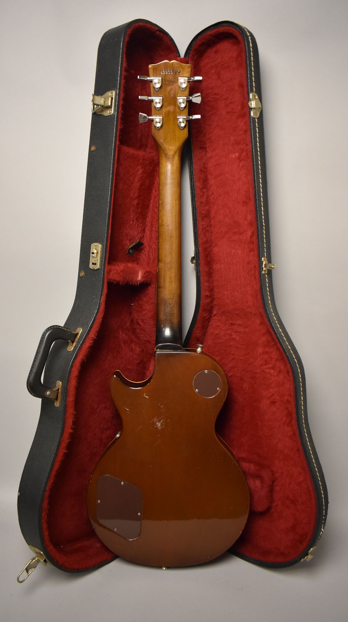 The back of a tobacco burst Les Paul, showing the headstock, neck, and body in its red-lined hard case.
