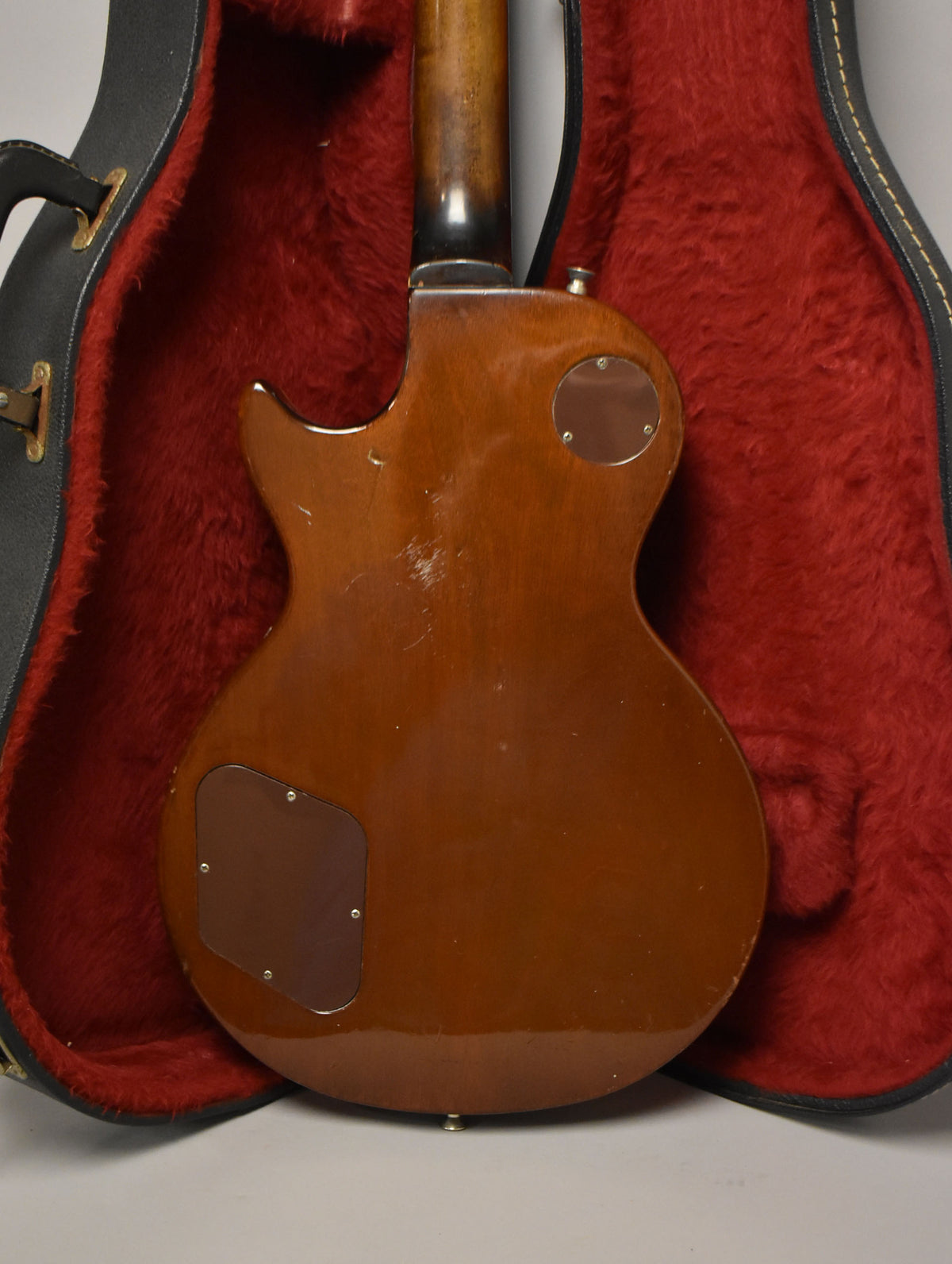 The guitar's tobacco burst back shows wear, with two brown control cavity covers, and is nestled in a red-lined case.