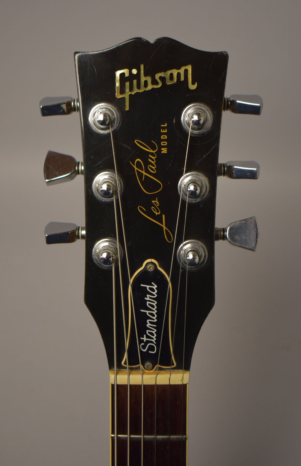 Close-up of the black headstock with gold lettering, chrome tuners, and visible scratches and finish wear.