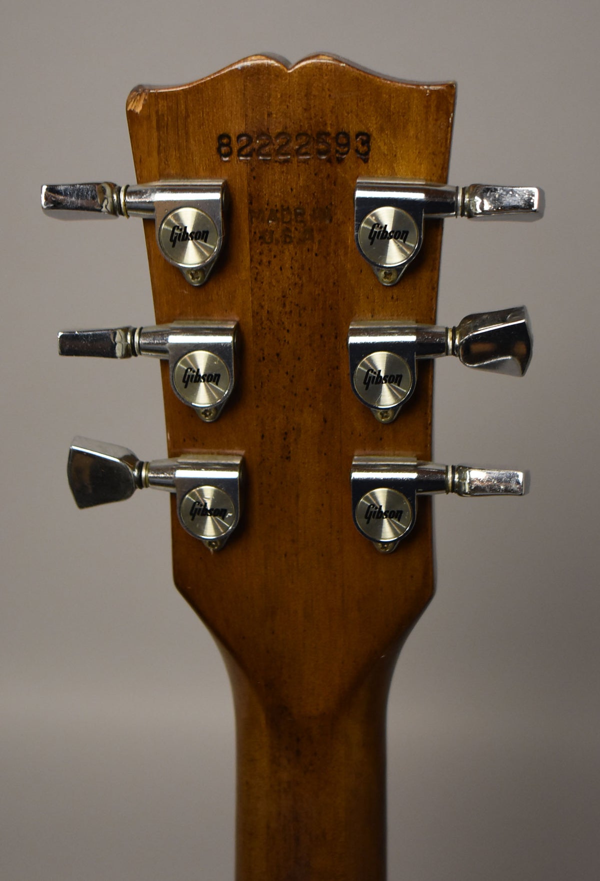 Rear view of the guitar's headstock and upper neck, showing six chrome tuners, a serial number, and some wear on the top edge.