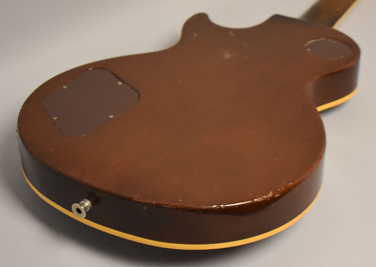 The guitar's dark brown back, with a control cavity cover, shows significant wear and chips along the bottom edge and input jack.