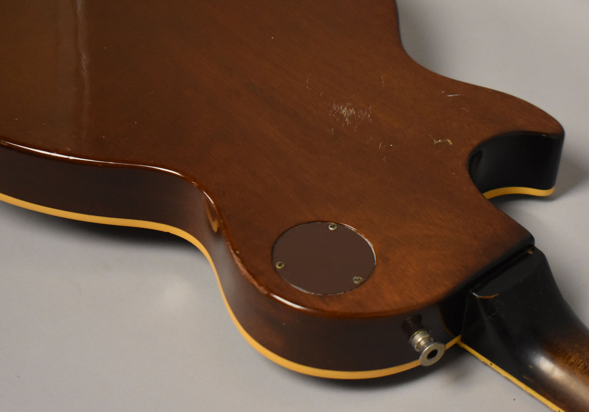Close-up of the guitar's lower back, showing the dark brown body with yellow binding, input jack, and a circular control plate.