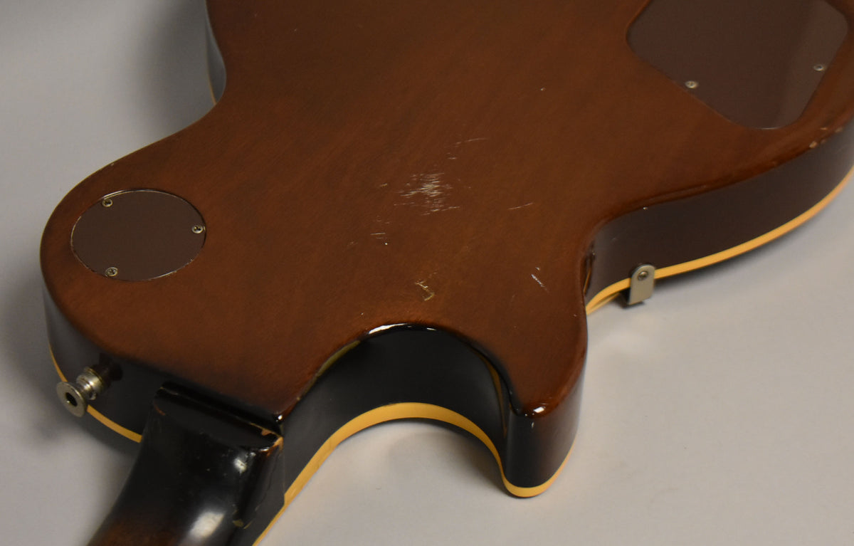 The back of a tobacco burst guitar, showing a round control cavity cover, output jack, and light scratches on the body.