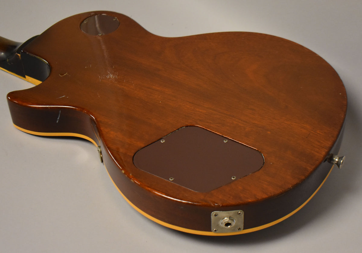 The back of the tobacco burst Les Paul shows a dark brown finish with visible scratches, a control cavity cover, and the output jack.