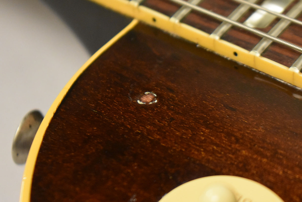 Close-up of the dark tobacco burst body, showing a circular ding with exposed wood, and a cream binding along the edge.