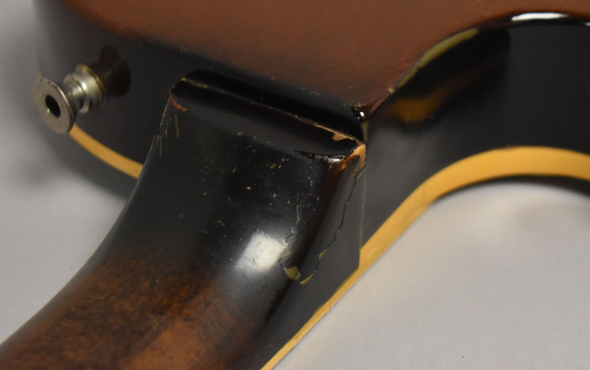 Close-up of the guitar's neck heel and lower bout, showing finish checking, chips, and wear on the black and tobacco burst finish.