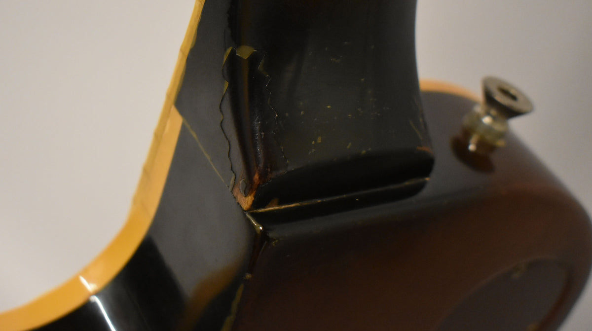 Close-up of the neck heel and upper body, showing heavy finish checking and wear on the black neck and tobacco burst body.