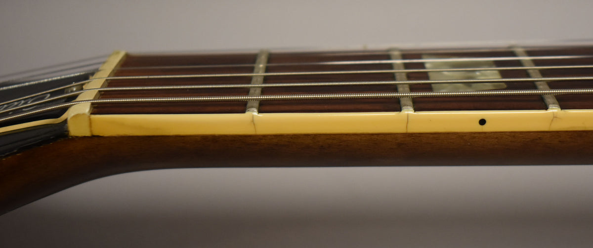 Close-up of the guitar's dark brown fretboard and cream binding, showing fret wires, block inlays, and a small black side dot.
