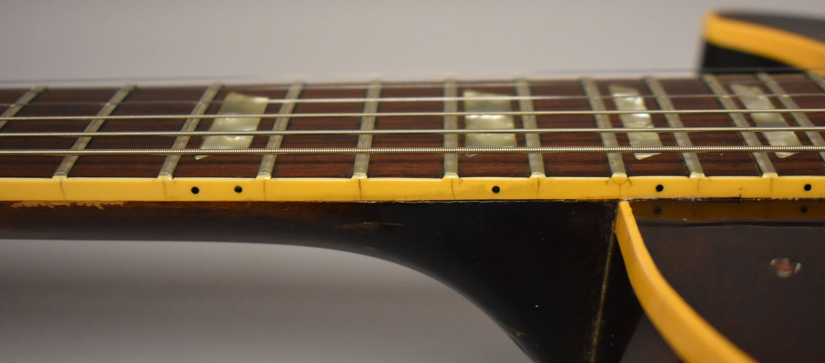 Close-up of the guitar's dark brown fretboard with trapezoid inlays, showing yellowed binding with checking and wear on the neck.