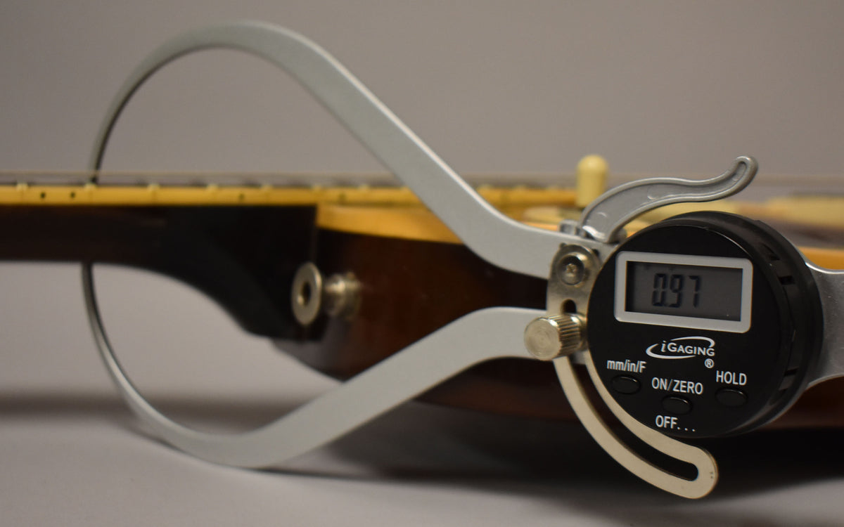 A digital caliper measures the guitar's neck relief at 0.97mm, showing the tobacco burst body and cream binding.