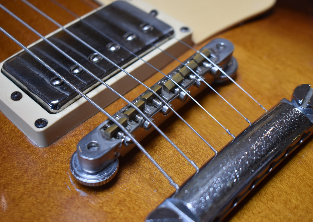 Close-up of the guitar's bridge, tailpiece, and bridge pickup, showing chrome hardware with some pitting and a tobacco burst finish.