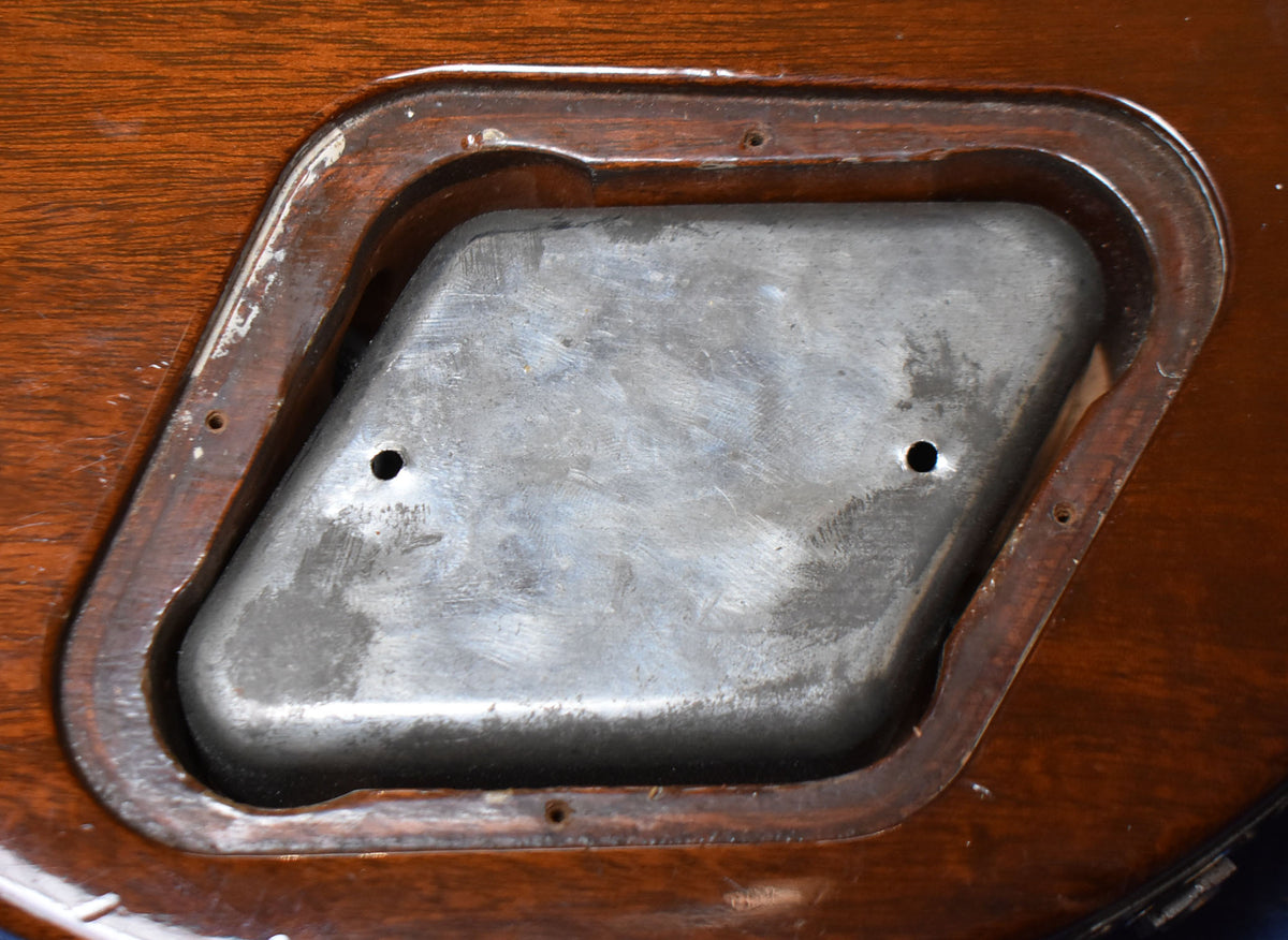 Close-up of the guitar's control cavity, showing a worn metal cover with two screw holes, surrounded by dark wood.