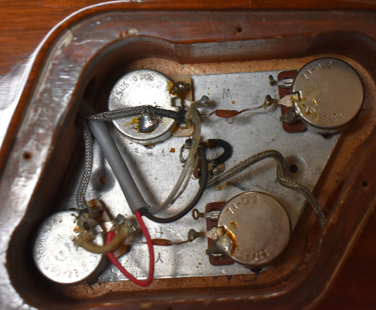 Close-up of the guitar's control cavity, revealing four tarnished silver potentiometers with visible wiring and solder joints on a metal plate.