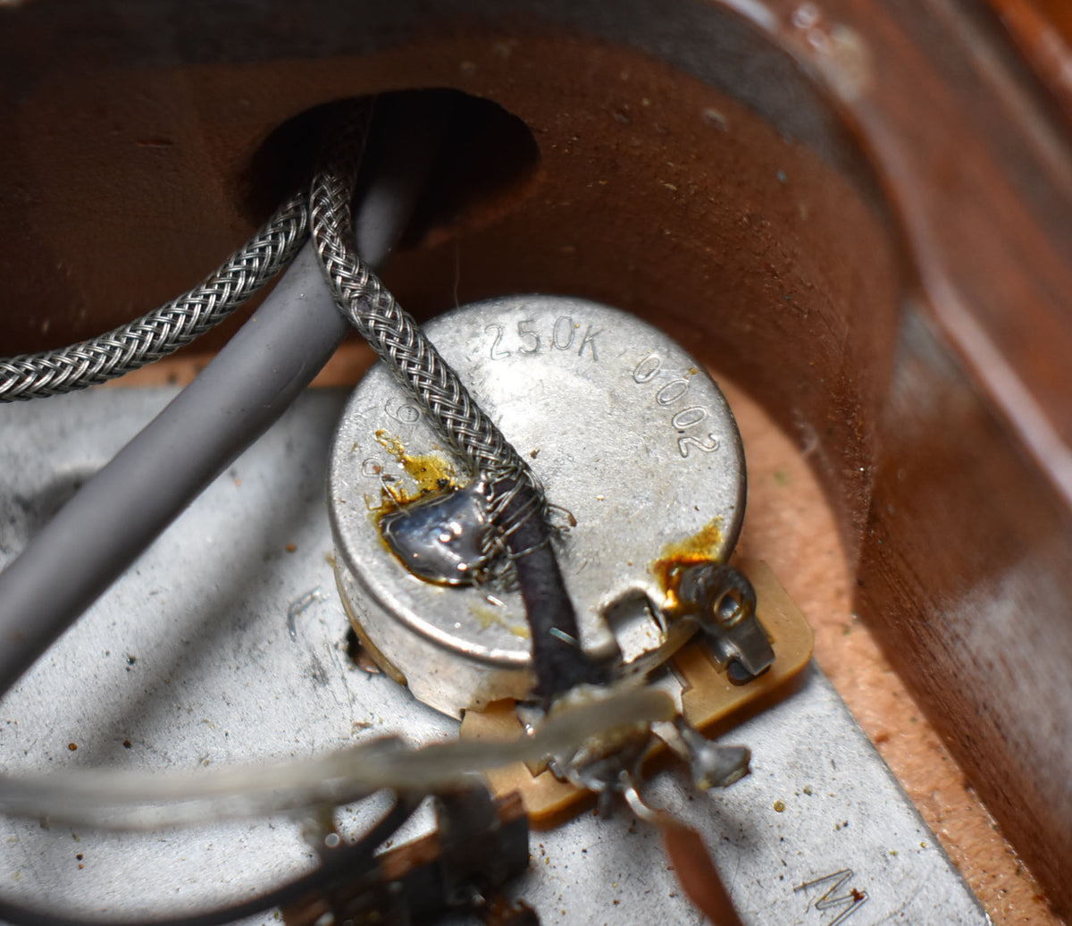 Close-up of the guitar's wiring cavity, showing a 250K potentiometer with soldered wires, some corrosion, and braided shielding.