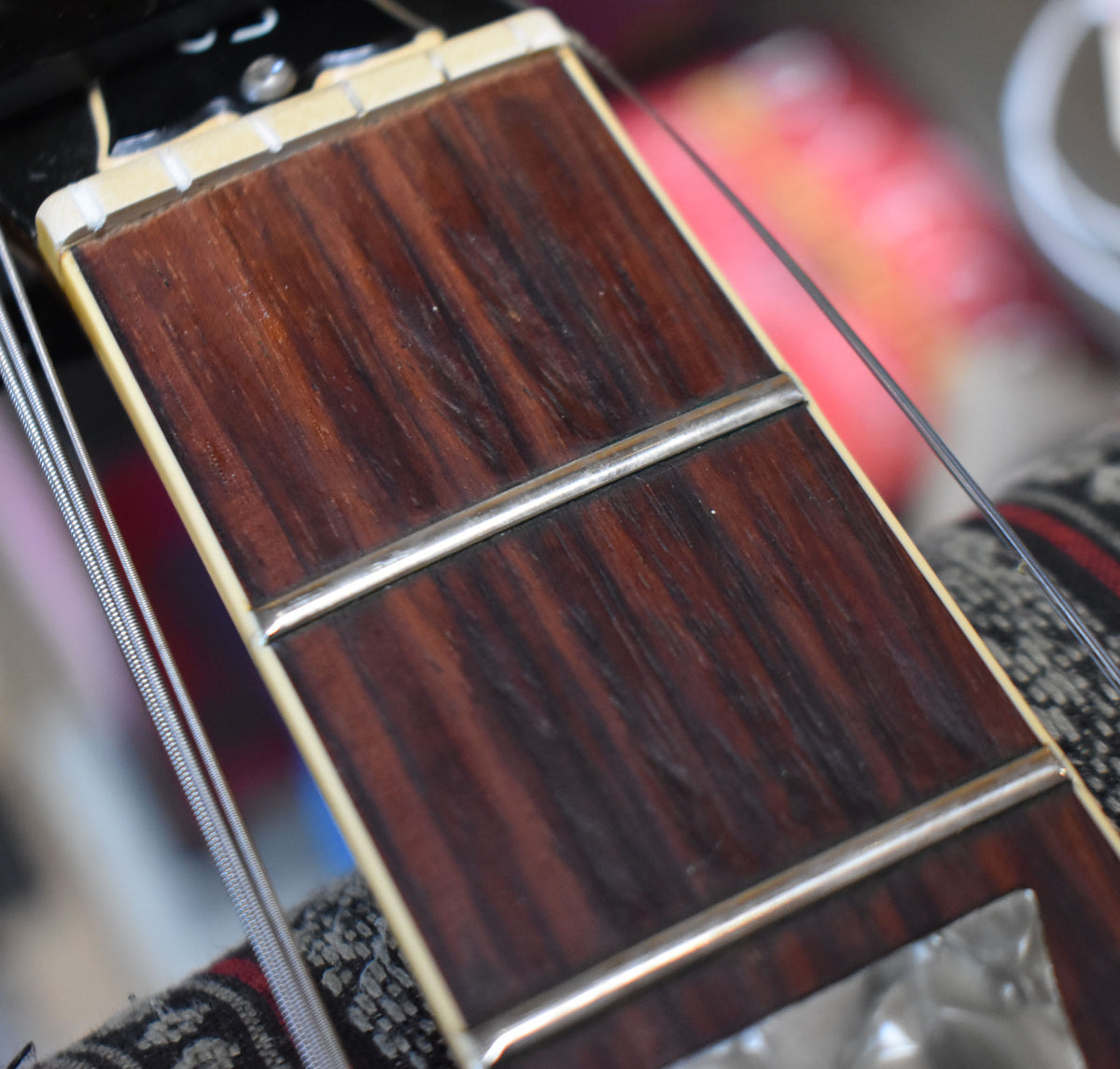 Close-up of the dark rosewood fretboard with cream binding, showing two frets, a nut, and a mother-of-pearl block inlay.