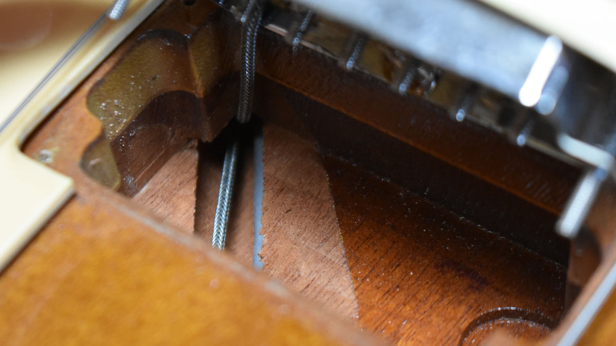 Close-up of the guitar's body, showing the strings passing through the dark wood of the bridge cavity, with some finish wear.