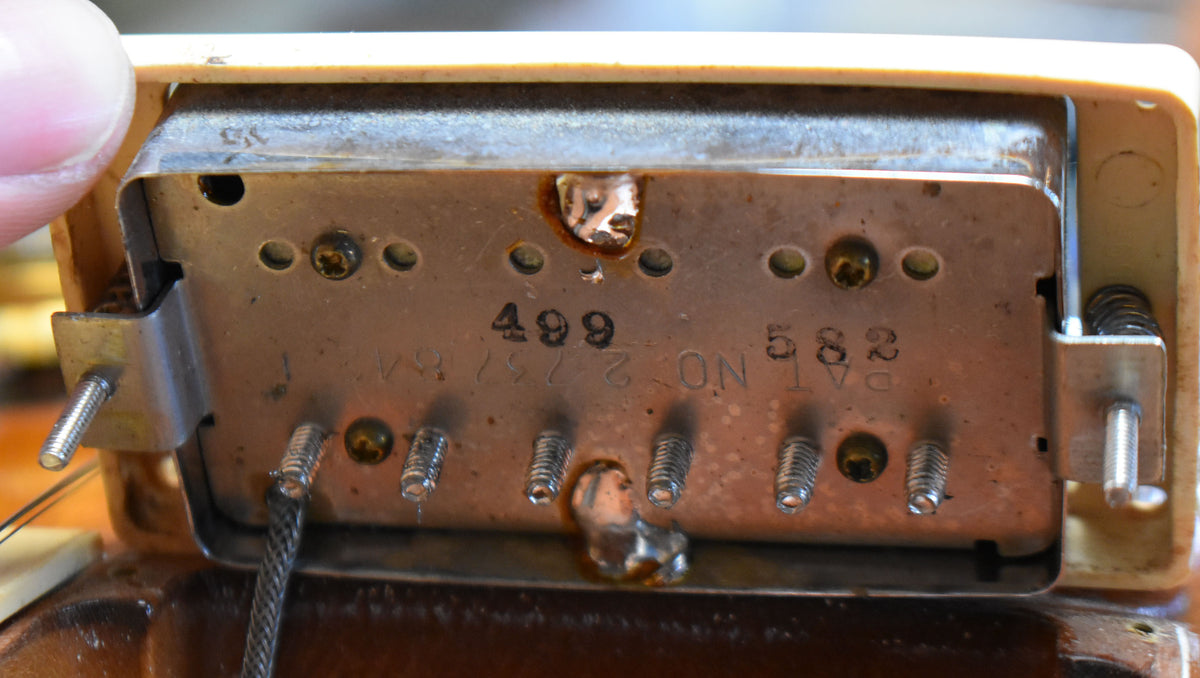 Close-up of the pickup's underside, showing the metal baseplate with visible solder joints, screws, and a braided wire.