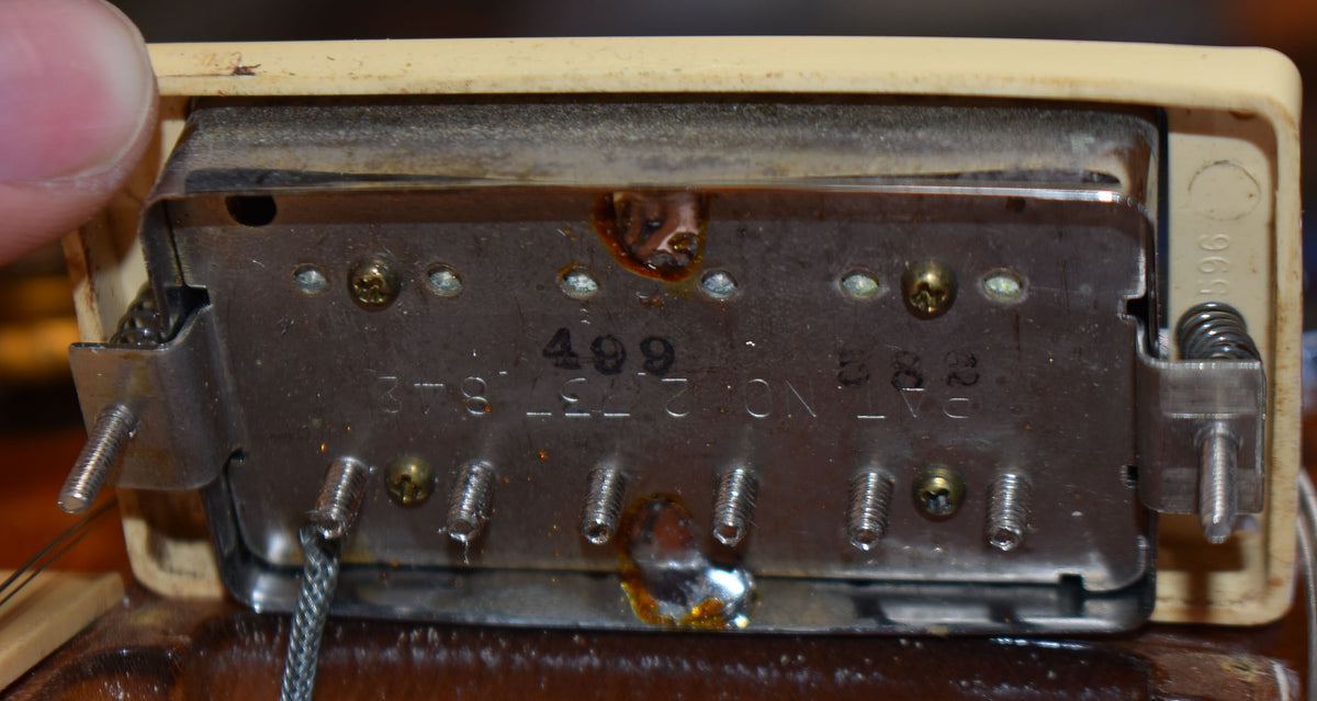 Close-up of the underside of a humbucker pickup, showing the metal baseplate with visible solder joints and mounting screws.