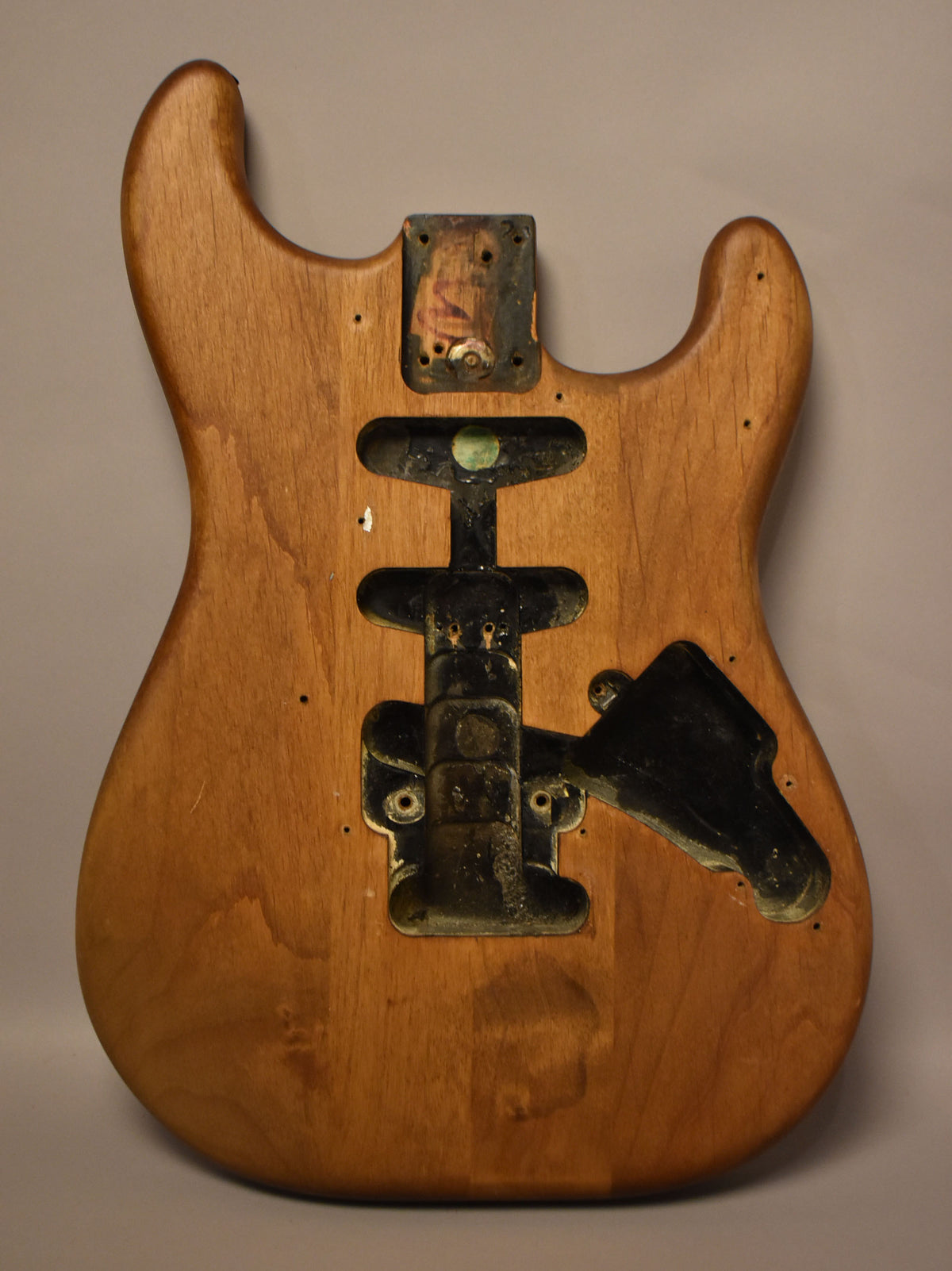 Full front view of a stripped natural wood Stratocaster body with dark, aged routing cavities and screw holes.
