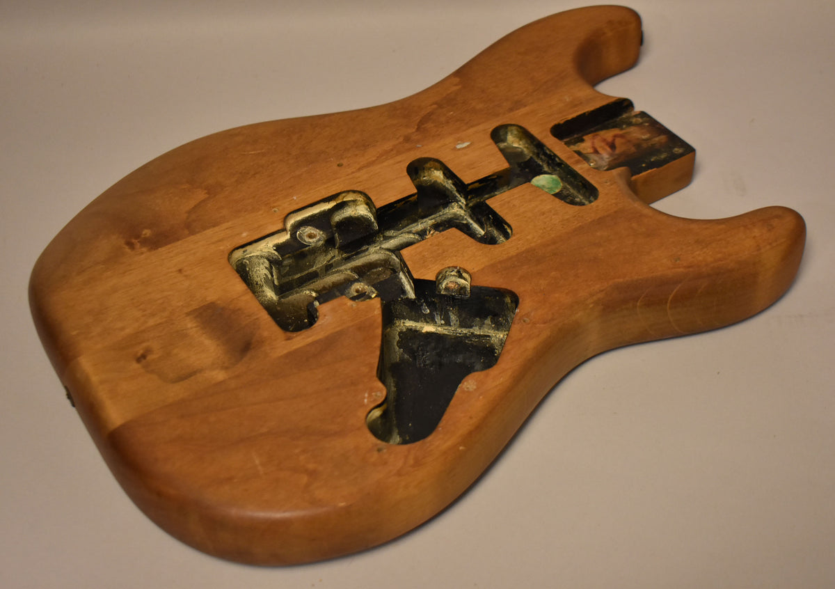 The stripped natural body is angled from the upper left, showing the front with black and yellow paint residue in the cavities.