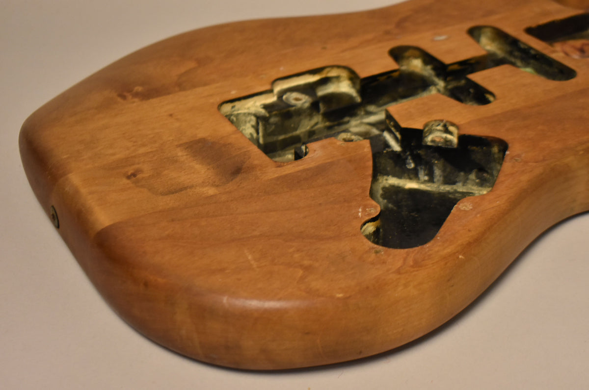 The stripped natural body, viewed from the lower bout, shows three pickup cavities with remnants of black and cream paint.
