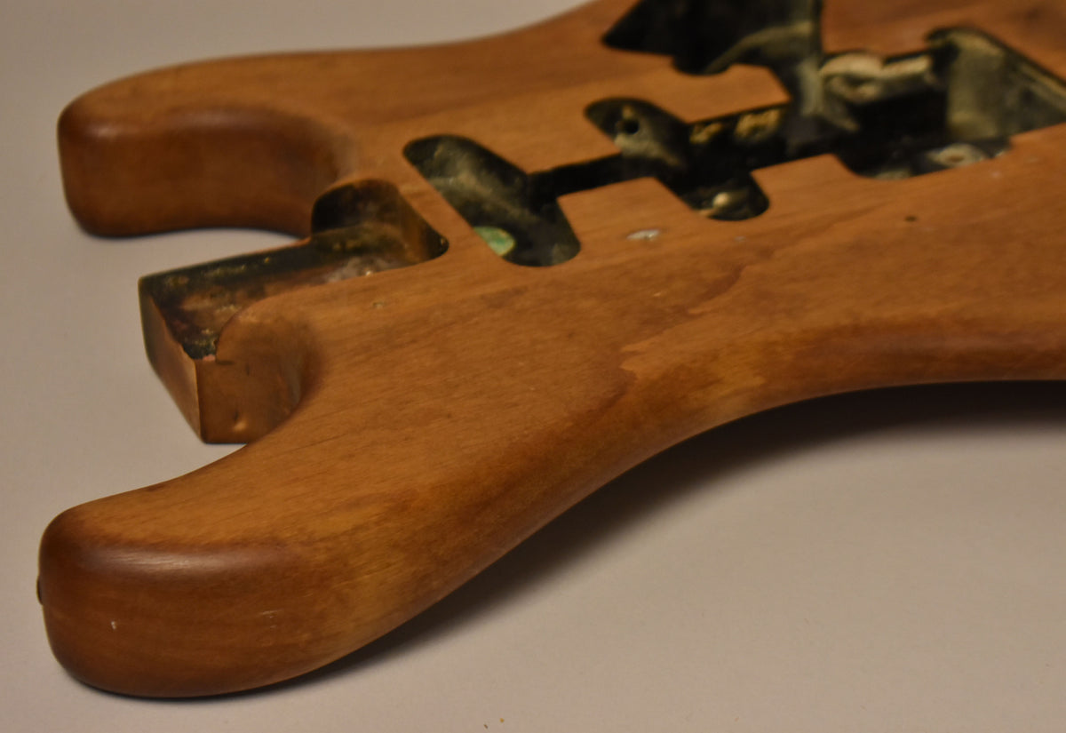 The stripped natural body, viewed from the lower bout, shows a light brown wood grain with dark, aged routing cavities.