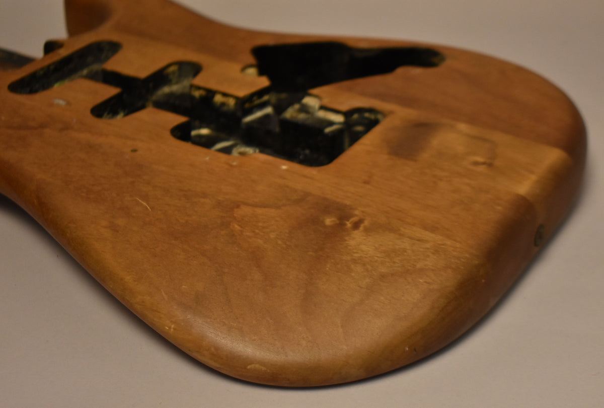 The stripped natural Stratocaster body is angled, showing the lower bout and tremolo cavity with visible wear and dark residue.
