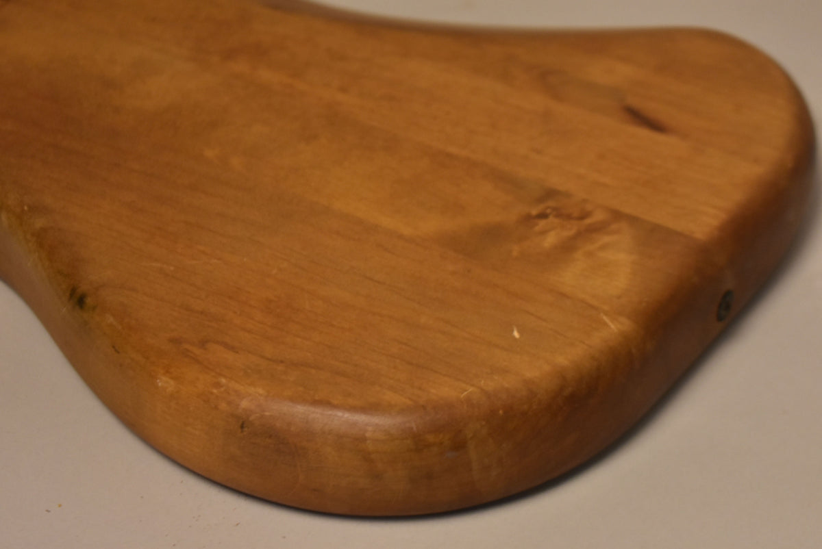 Close-up of the lower bout of a stripped natural wood Stratocaster body, showing grain, minor dings, and a screw hole on the side.
