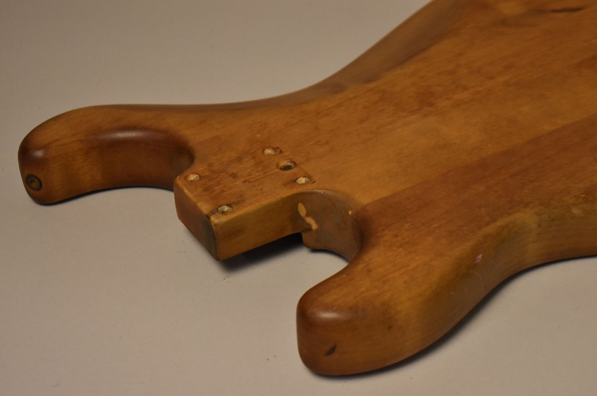 The stripped natural Stratocaster body is angled, showing the neck pocket with four screw holes and a chipped finish on the lower horn.