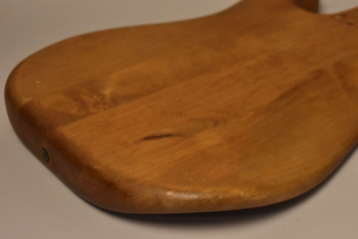 The lower bout of a stripped natural Stratocaster body, showing a dark streak in the wood grain and minor edge wear.