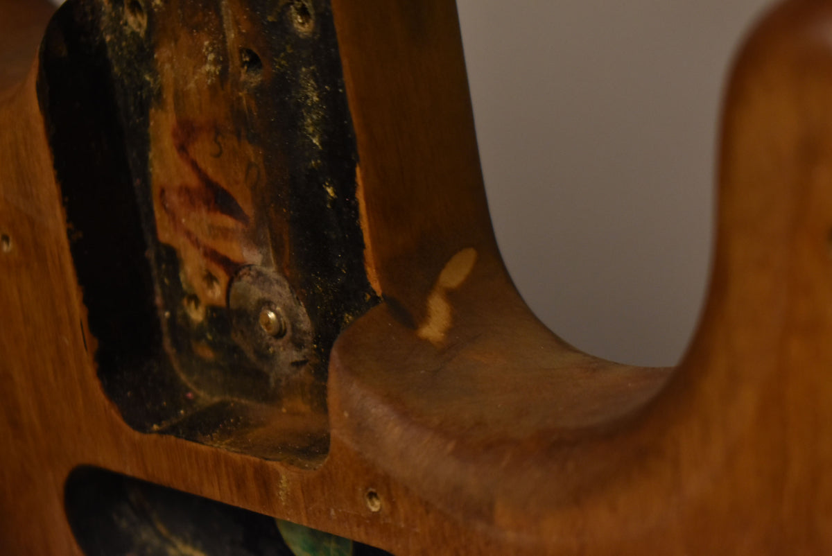 Close-up of the natural wood body's neck pocket, showing dark residue, screw holes, and a light patch of wear on the upper horn.