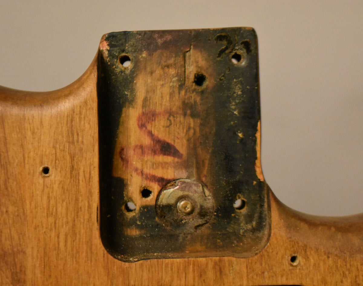 Close-up of the natural wood body's neck pocket, showing dark residue, four screw holes, and a worn metal plate with a screw.