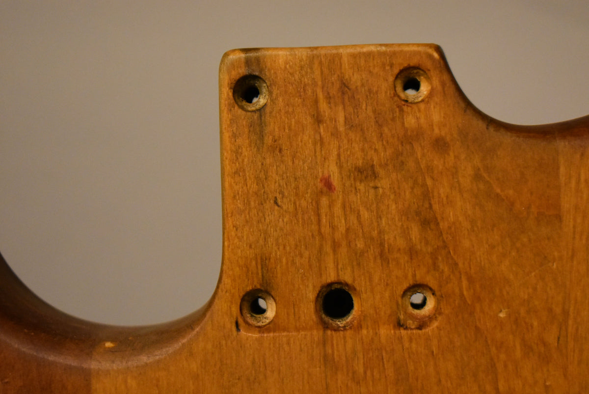 Close-up of the natural-finished body's neck pocket, showing four neck screw holes and three control holes, with some red staining.