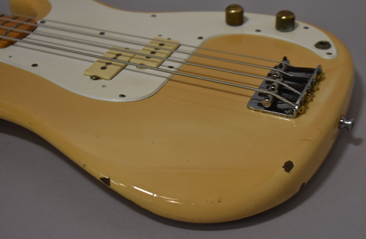 Close-up of the bass body, showing the aged white finish, white pickguard, chrome bridge, and two brass control knobs, with visible chips and wear.