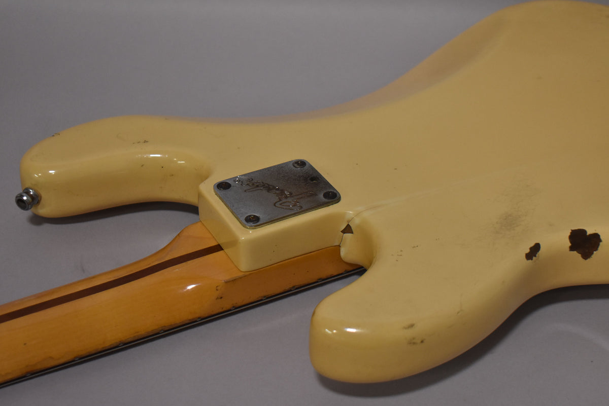The back of a vintage white bass shows a worn neck plate, a strap button, and significant paint chips on the body.