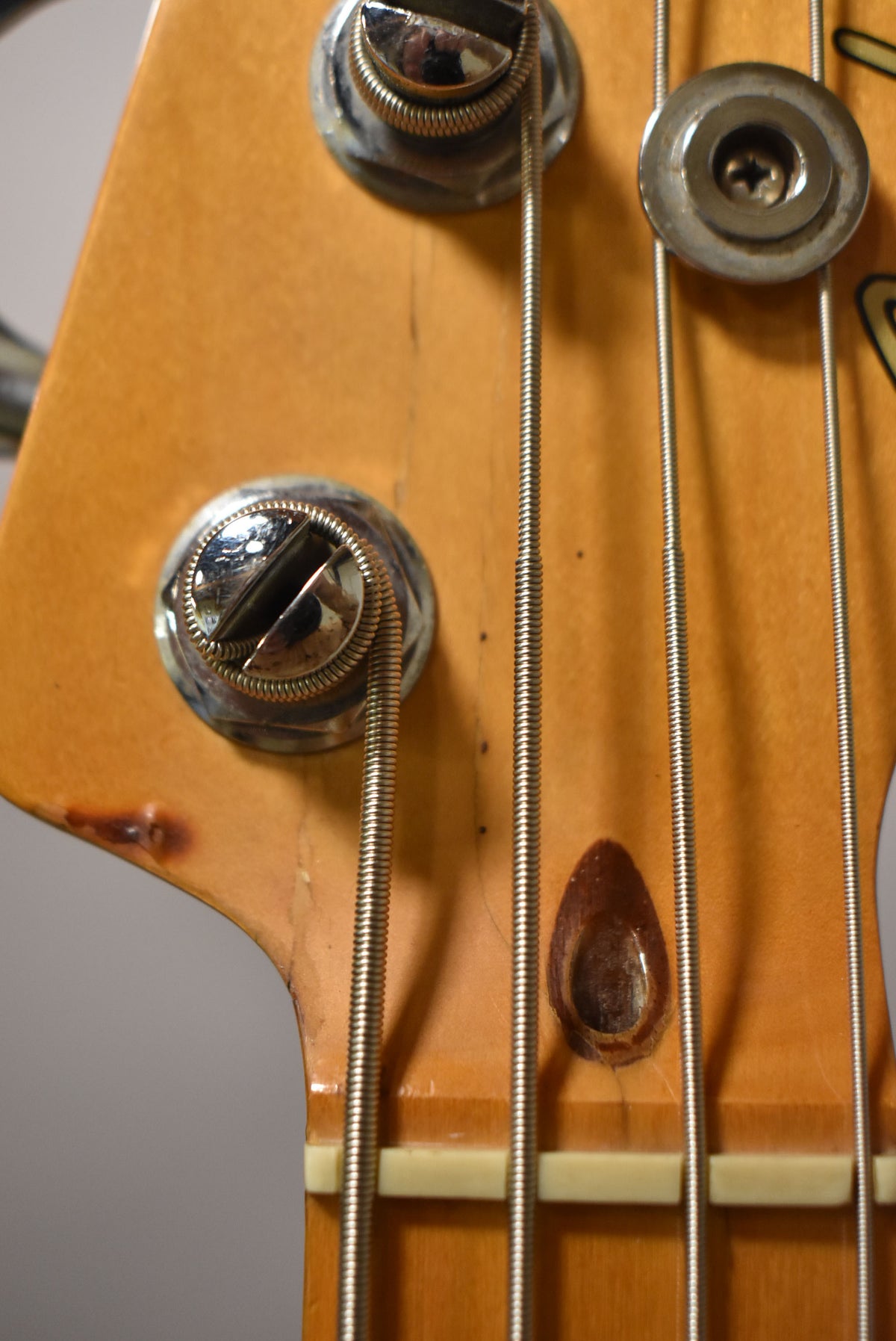 Close-up of a bass guitar headstock, showing three tuning pegs, four strings, a string tree, and the top of the nut.