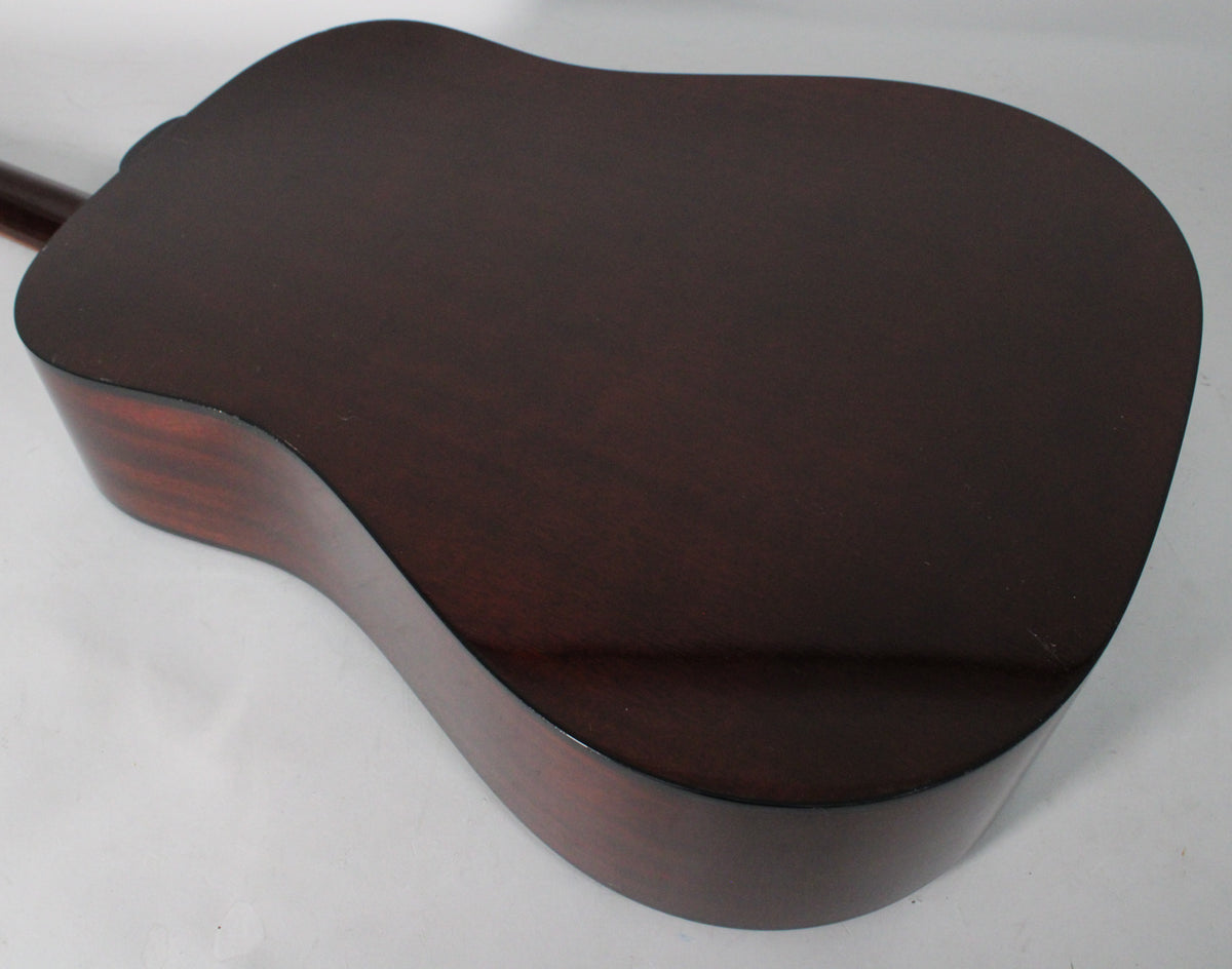 The dark sunburst acoustic guitar's back and side are visible, showing a few light scratches on the lower bout.