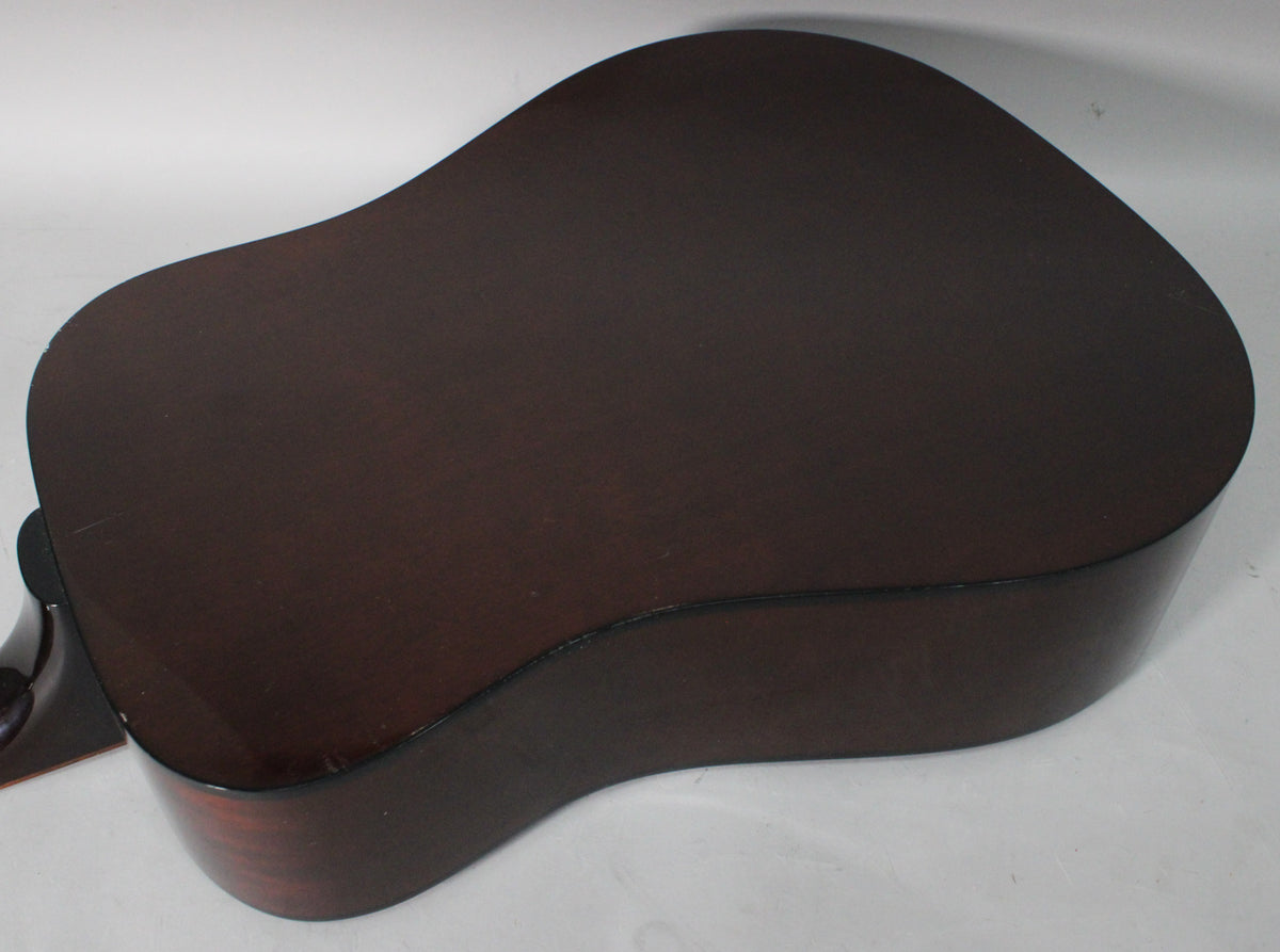 The back of the sunburst acoustic guitar is visible, showing a dark brown finish with some light scratches and a small chip near the neck joint.
