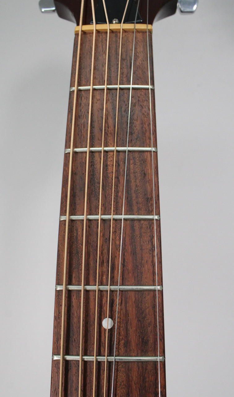 Close-up of the dark brown fretboard with six strings and a single white dot inlay at the seventh fret.