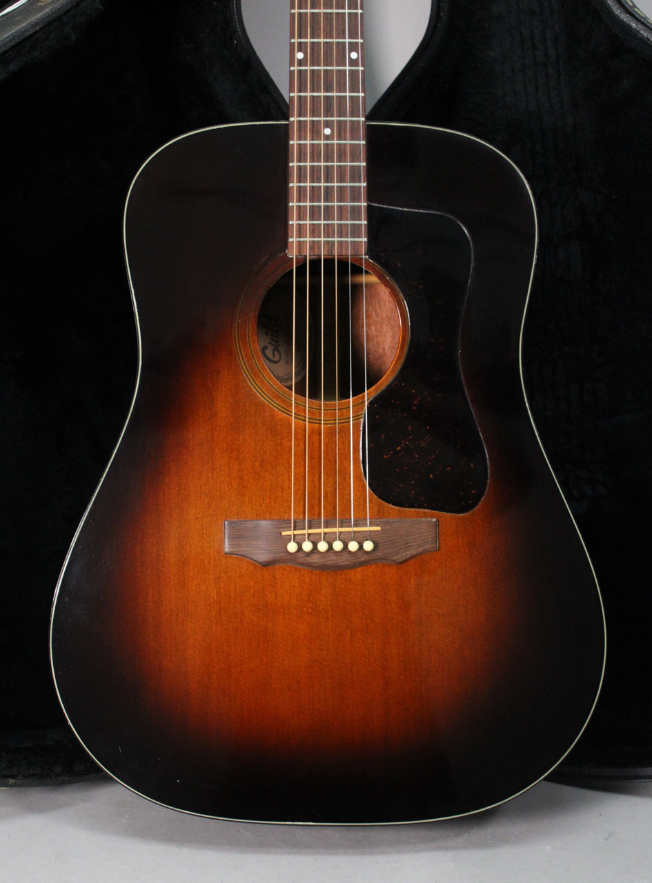 Full-frame front view of a sunburst acoustic guitar with a dark pickguard, showing light wear on the body.