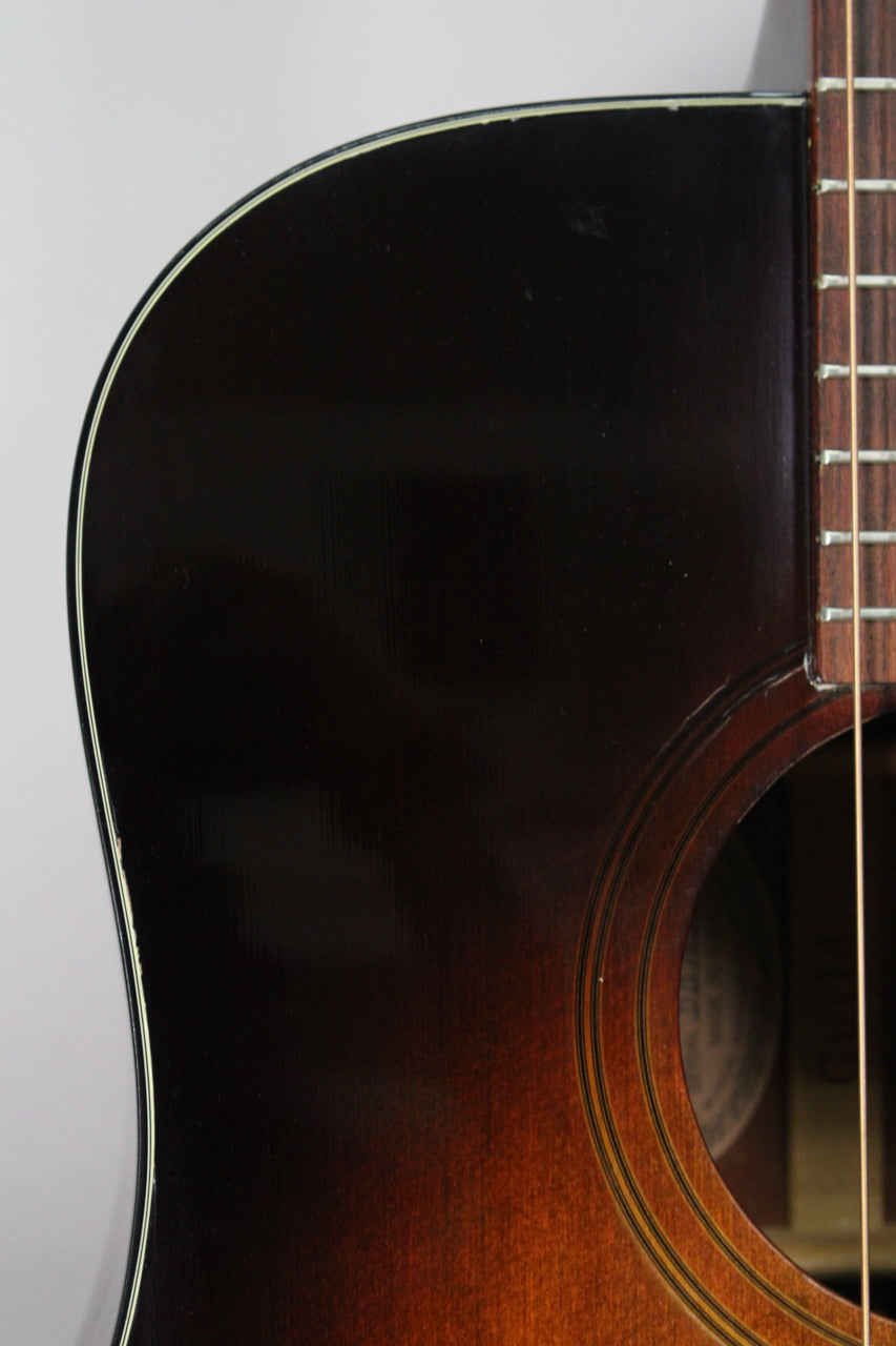 Close-up of the guitar's upper bout, showing the dark sunburst finish, white binding, and soundhole with concentric rings.