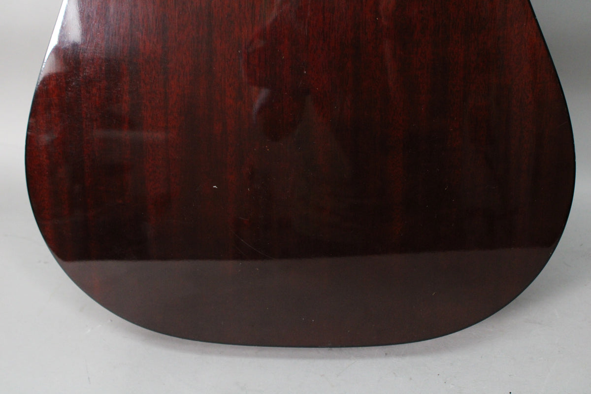 The lower back of the guitar shows a dark sunburst finish with visible wood grain, light scratches, and a few small white flecks.