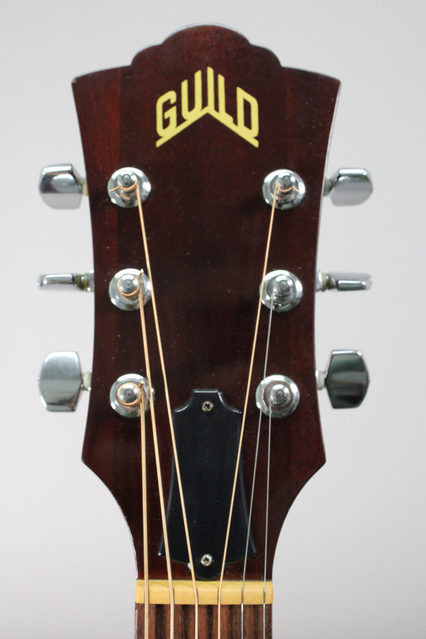 Close-up of the dark brown headstock with six chrome tuners, a black truss rod cover, and light-colored strings.