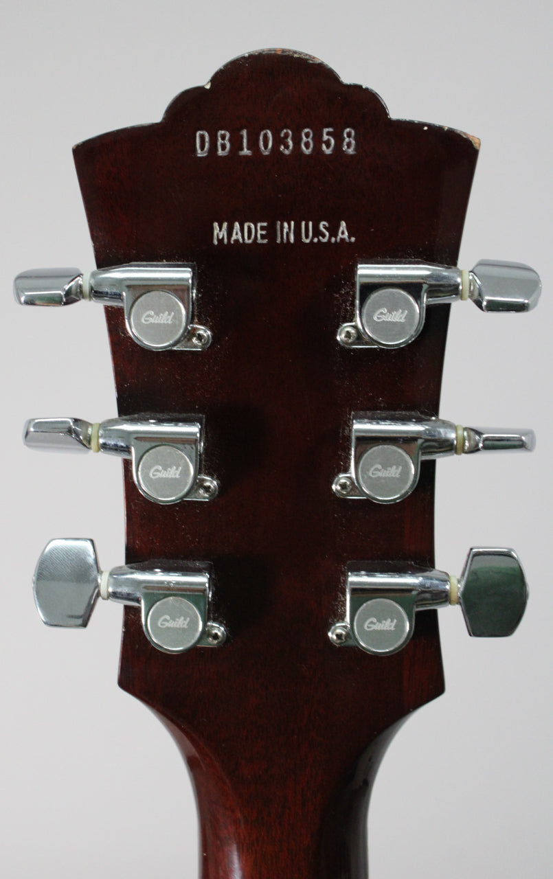 The back of the guitar's dark brown headstock, showing six chrome tuners and "DB103858 MADE IN U.S.A." stamped into the wood.