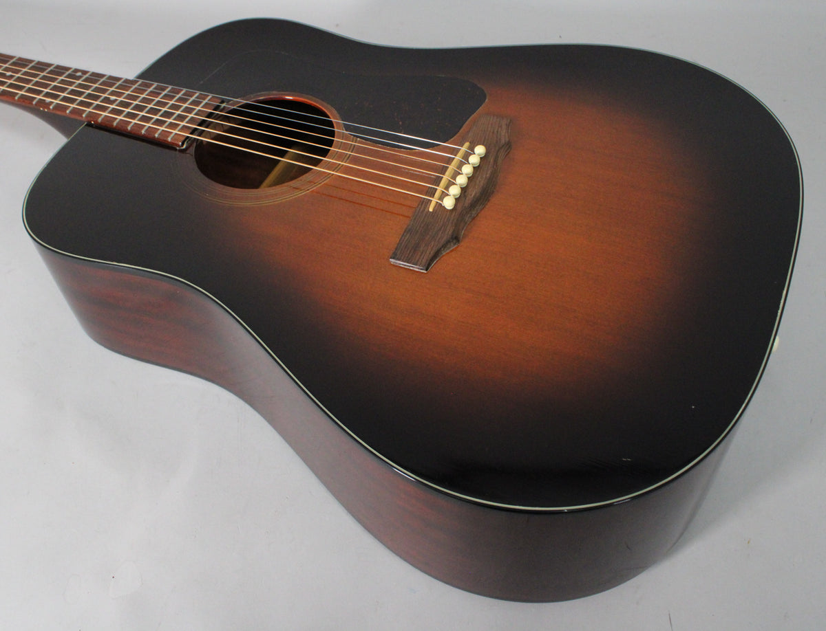 The sunburst acoustic guitar is angled from the upper left, showing the dark brown to amber body, pickguard, and bridge.