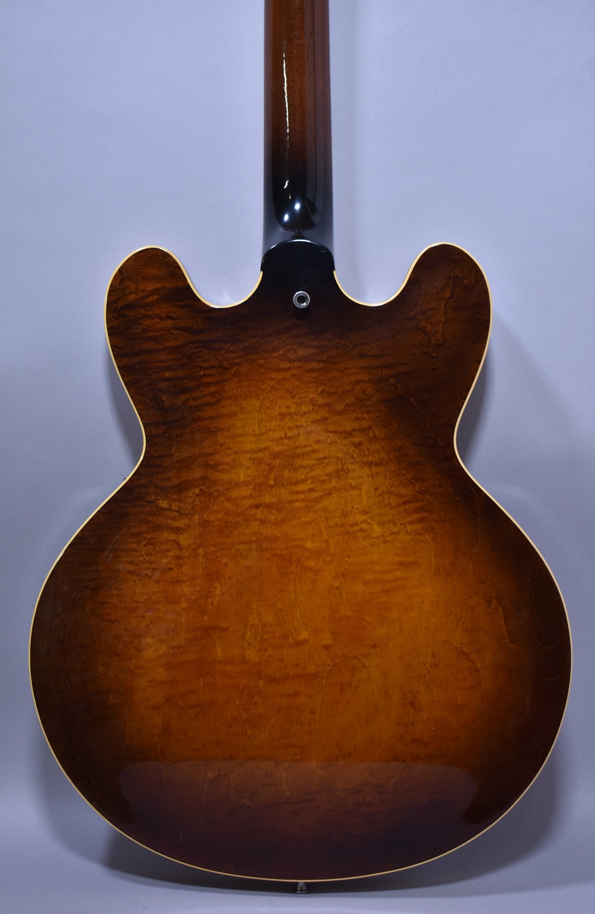 The guitar's flame maple back shows a rich sunburst finish, with a strap button visible at the neck heel.
